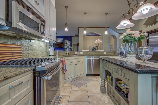 kitchen with appliances with stainless steel finishes, arched walkways, tasteful backsplash, stone countertops, and light tile patterned floors