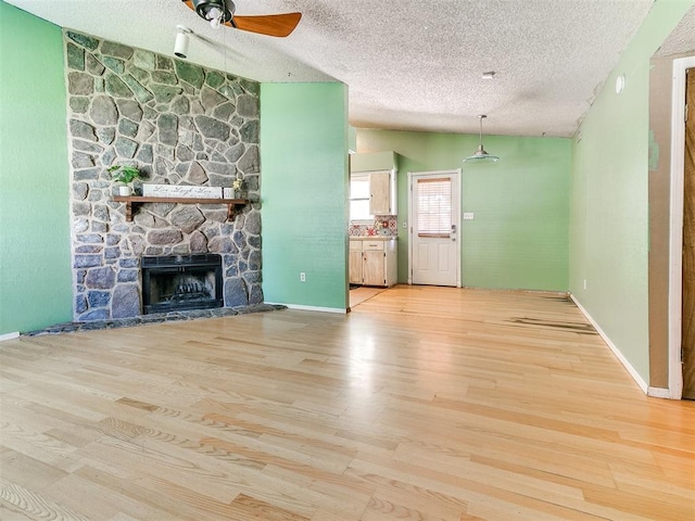 1916 Twin Tree Dr, Norman, OK 73071 - unfurnished living room with a ceiling fan, a textured ceiling, wood finished floors, vaulted ceiling, and a stone fireplace
