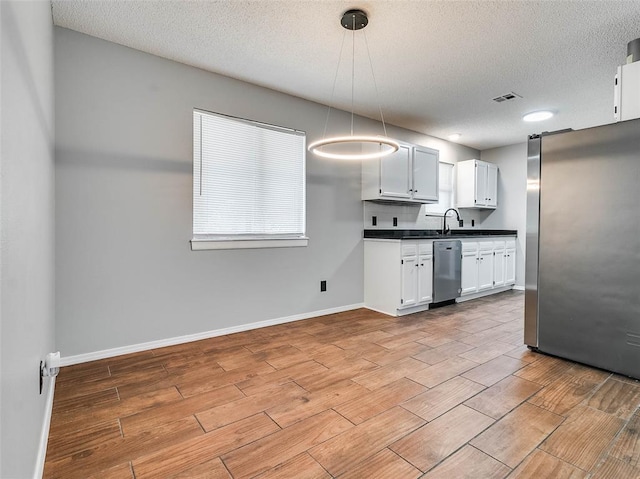 1810 Spring Ave, Stroud, OK 74079 - kitchen featuring stainless steel appliances, wood tiled floors, dark countertops, a textured ceiling, and white cabinets