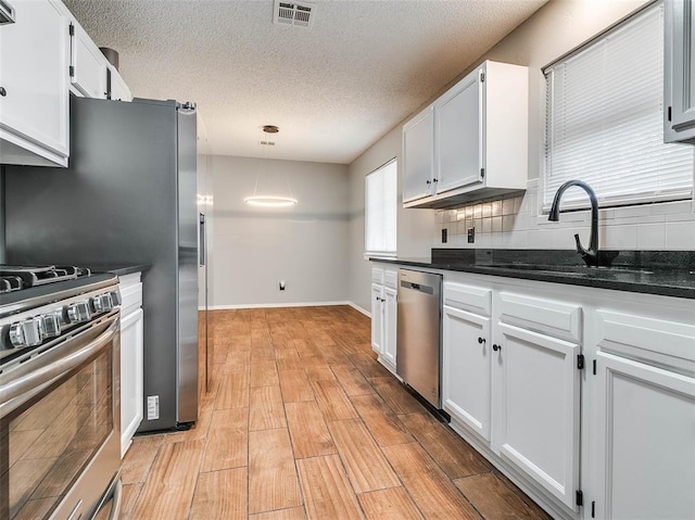 1810 Spring Ave, Stroud, OK 74079 - kitchen featuring appliances with stainless steel finishes, white cabinetry, backsplash, light wood-style floors, and a textured ceiling