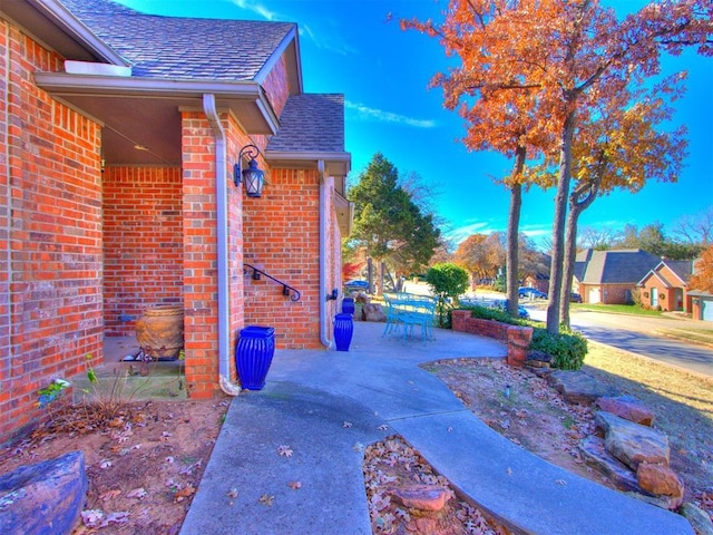 2404 Pawnee Xing, Edmond, OK 73034 - view of property exterior featuring roof with shingles, brick siding, and a patio area