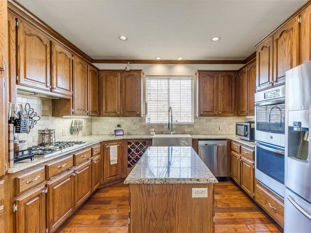 2404 Pawnee Xing, Edmond, OK 73034 - kitchen with appliances with stainless steel finishes, a kitchen island, decorative backsplash, dark wood-style floors, and ornamental molding