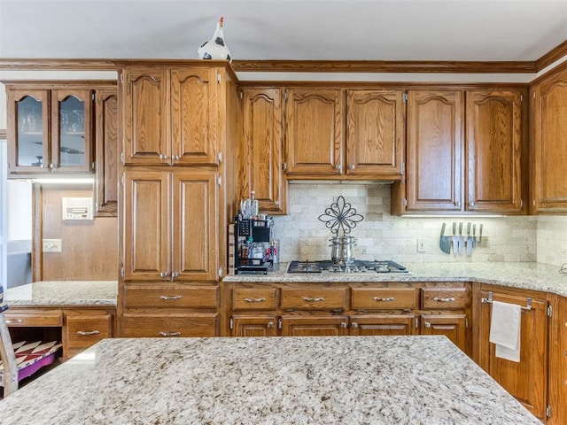 2404 Pawnee Xing, Edmond, OK 73034 - kitchen with stainless steel gas cooktop, brown cabinets, light stone countertops, and decorative backsplash