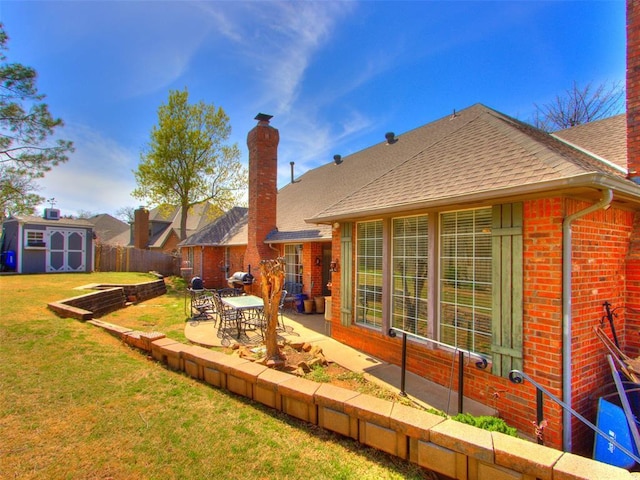 2404 Pawnee Xing, Edmond, OK 73034 - rear view of house featuring a shingled roof, a patio, brick siding, a shed, and a chimney