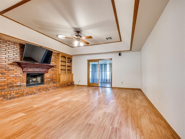 1917 Goldenrod Ln, Midwest City, OK 73130 - unfurnished living room featuring a tray ceiling, wood finished floors, ceiling fan, built in shelves, and a fireplace