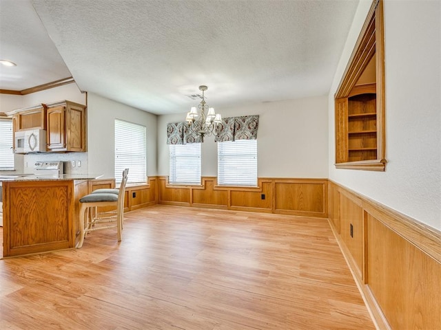 1917 Goldenrod Ln, Midwest City, OK 73130 - dining space featuring light wood-type flooring, wainscoting, a textured ceiling, a chandelier, and crown molding