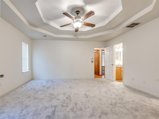 1917 Goldenrod Ln, Midwest City, OK 73130 - unfurnished bedroom featuring a tray ceiling, light carpet, ensuite bath, and a ceiling fan