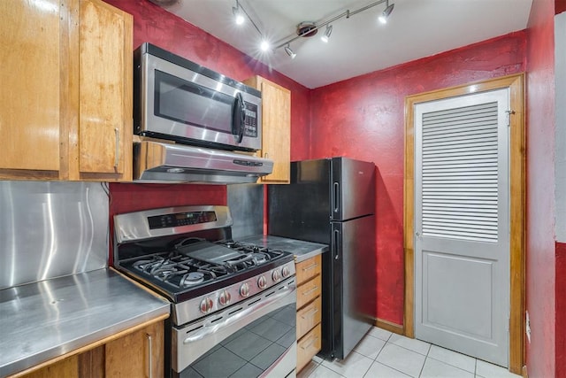 2527 NW 62nd St Unit 214, Oklahoma City, OK 73112 - kitchen with stainless steel countertops, stainless steel appliances, under cabinet range hood, light tile patterned flooring, and brown cabinetry