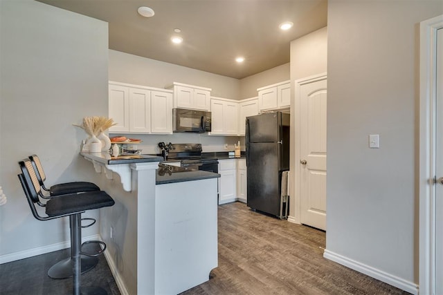 1010 SW 91st St, Oklahoma City, OK 73139 - kitchen featuring black appliances, a peninsula, a breakfast bar, white cabinets, and dark countertops