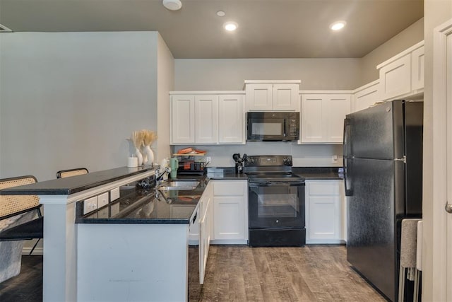 1010 SW 91st St, Oklahoma City, OK 73139 - kitchen featuring black appliances, a peninsula, wood finished floors, white cabinetry, and a kitchen breakfast bar