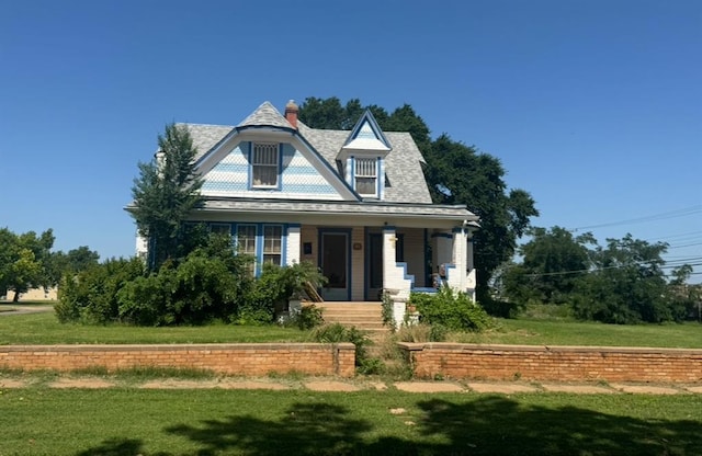 victorian-style house featuring covered porch, a front lawn, and a chimney