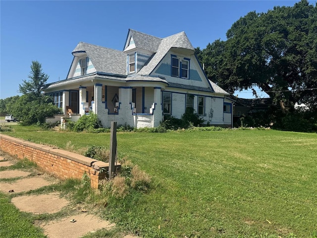 view of front facade with covered porch, a front yard, and a shingled roof