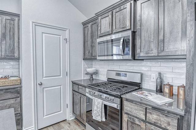12712 NW 4th St, Yukon, OK 73099 - kitchen with appliances with stainless steel finishes, vaulted ceiling, tasteful backsplash, light wood-style flooring, and dark countertops