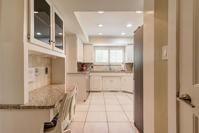 1810 Sandpiper Dr, Edmond, OK 73034 - kitchen featuring decorative backsplash, light stone counters, glass insert cabinets, light tile patterned floors, and recessed lighting