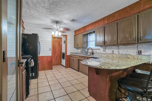1108 S 13th St, Clinton, OK 73601 - kitchen with a peninsula, a ceiling fan, a breakfast bar area, wood walls, and light tile patterned floors