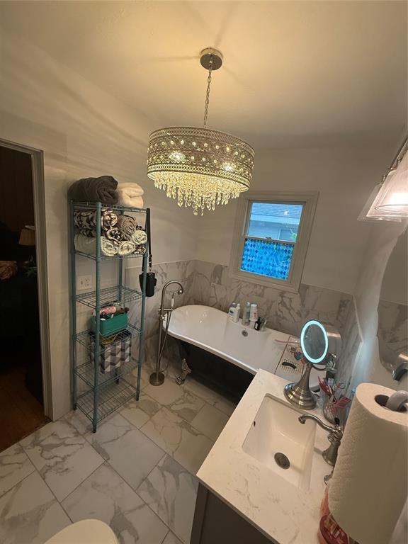 1522 S 9th St, Chickasha, OK 73018 - full bath with marble look tile flooring, vanity, a freestanding tub, tile walls, and a chandelier
