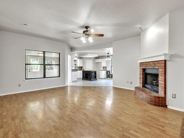 4001 Tori Pl, Yukon, OK 73099 - unfurnished living room with ceiling fan, light wood-style flooring, healthy amount of natural light, a fireplace, and a textured ceiling