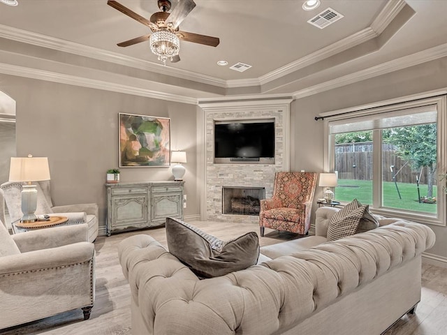 16117 Cale Dr, Edmond, OK 73013 - living area featuring ceiling fan, light wood-style flooring, a large fireplace, a raised ceiling, and ornamental molding