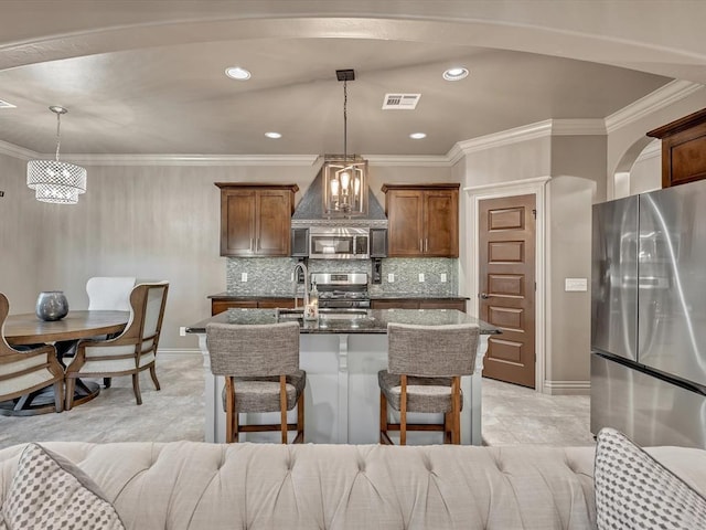 16117 Cale Dr, Edmond, OK 73013 - kitchen with appliances with stainless steel finishes, dark stone counters, wall chimney exhaust hood, a kitchen island with sink, and hanging light fixtures