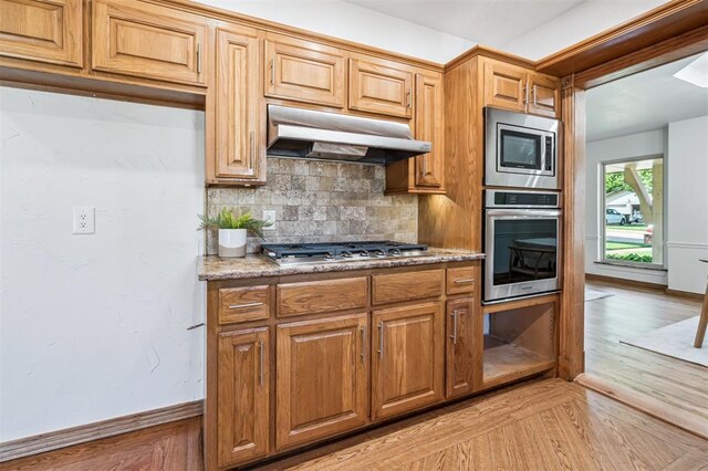 3425 Cheyenne Dr, Edmond, OK 73013 - kitchen with stainless steel appliances, under cabinet range hood, backsplash, light wood finished floors, and light stone countertops