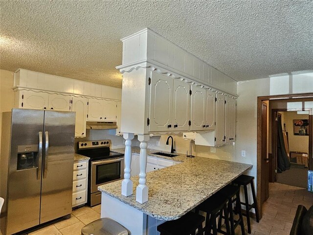 321 W 4th St, Hobart, OK 73651 - kitchen with appliances with stainless steel finishes, under cabinet range hood, a textured ceiling, a peninsula, and a breakfast bar area