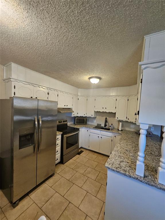 321 W 4th St, Hobart, OK 73651 - kitchen featuring appliances with stainless steel finishes, a textured ceiling, light tile patterned floors, white cabinetry, and light stone counters