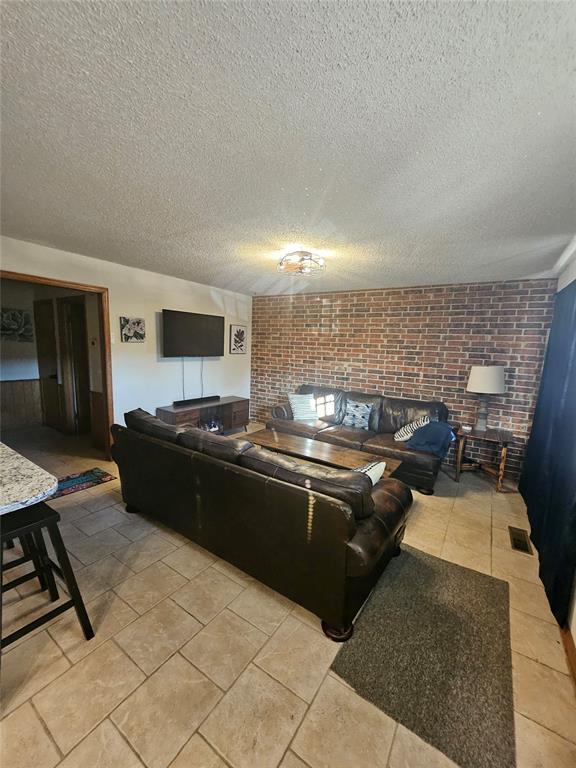 321 W 4th St, Hobart, OK 73651 - living area with brick wall, a textured ceiling, and light tile patterned floors