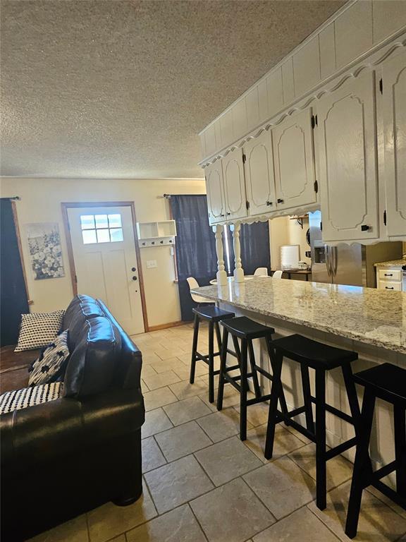 321 W 4th St, Hobart, OK 73651 - kitchen with white cabinets, a textured ceiling, light stone counters, and a kitchen bar