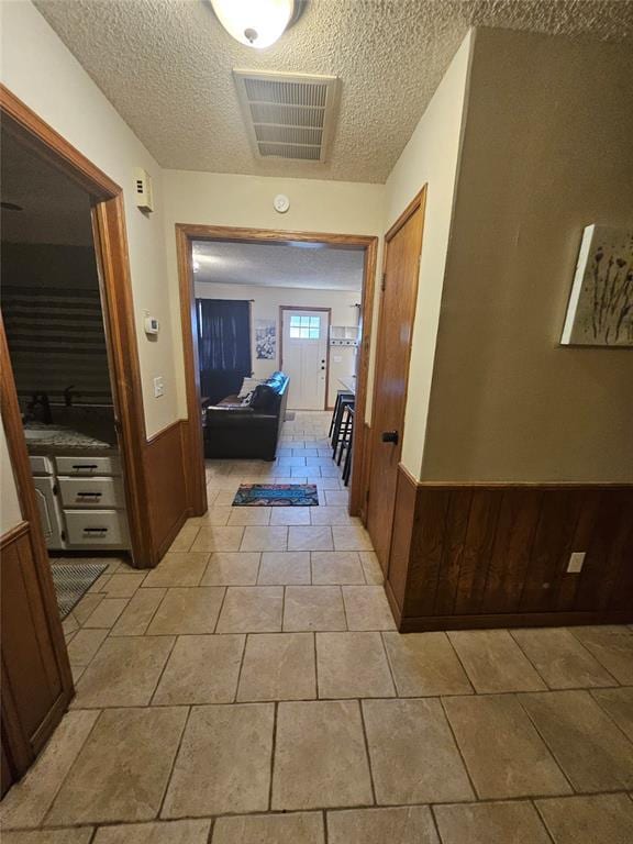 321 W 4th St, Hobart, OK 73651 - corridor featuring a wainscoted wall, a textured ceiling, wood walls, and light tile patterned floors