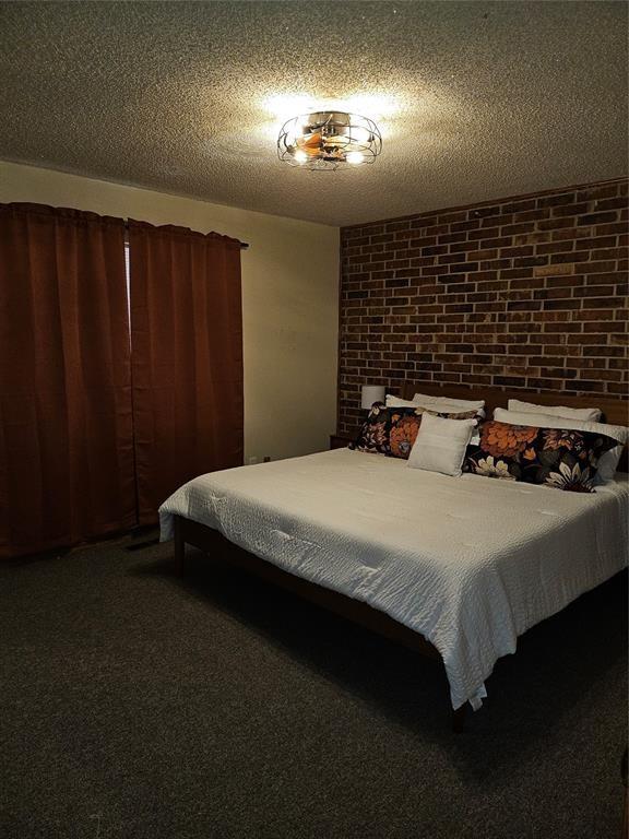 321 W 4th St, Hobart, OK 73651 - carpeted bedroom with brick wall and a textured ceiling