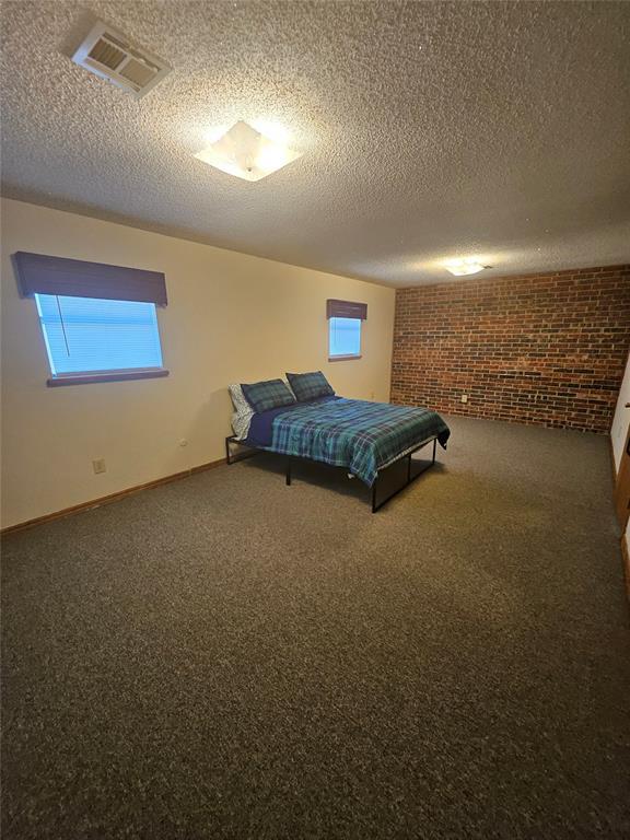 321 W 4th St, Hobart, OK 73651 - bedroom with brick wall, carpet flooring, and a textured ceiling