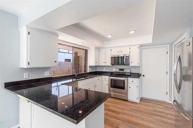 2104 Brookhaven Dr, Edmond, OK 73034 - kitchen featuring stainless steel appliances, a peninsula, a raised ceiling, dark stone counters, and white cabinetry