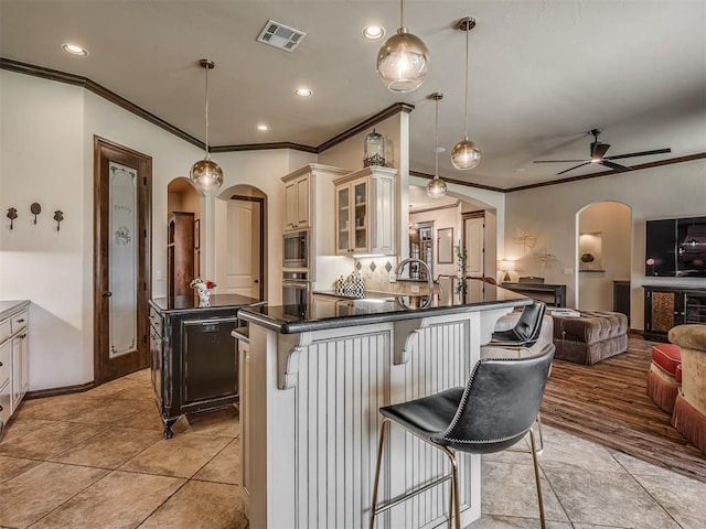 16208 Windrush Pl, Edmond, OK 73013 - kitchen with arched walkways, cream cabinets, appliances with stainless steel finishes, dark countertops, and ornamental molding