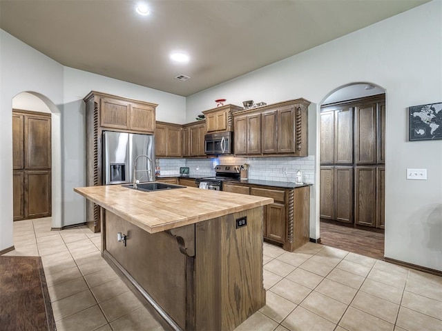 749 Dana Dr, Yukon, OK 73099 - kitchen featuring appliances with stainless steel finishes, wooden counters, arched walkways, light tile patterned flooring, and backsplash