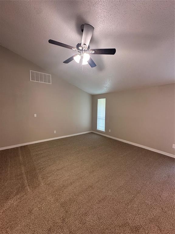 8317 NW 85th St, Oklahoma City, OK 73132 - empty room with a textured ceiling, dark colored carpet, a ceiling fan, and vaulted ceiling