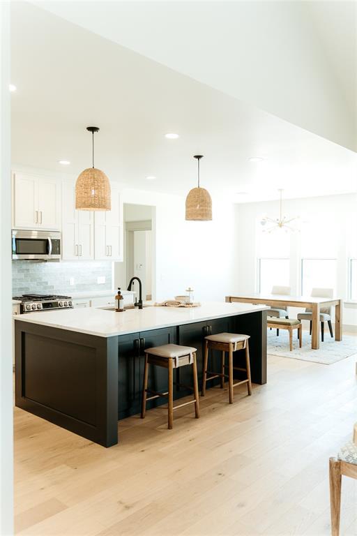 2741 Two Socks Run, Guthrie, OK 73044 - kitchen featuring stainless steel appliances, white cabinetry, backsplash, light wood finished floors, and a large island with sink