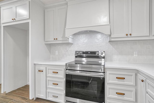1608 Truman Dr, Altus, OK 73521 - kitchen with stainless steel range with electric stovetop, custom exhaust hood, wood finished floors, white cabinets, and tasteful backsplash