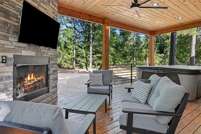 42 Hickory Ridge Rd, Broken Bow, OK 74728 - deck featuring a hot tub, view of wooded area, a ceiling fan, and an outdoor living space with a fireplace