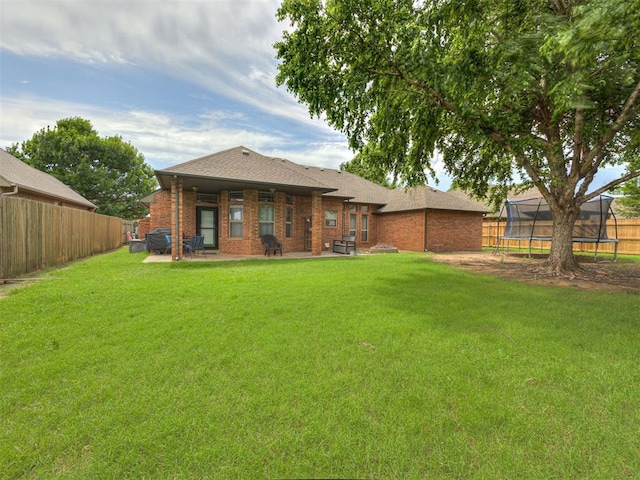 2108 Mulberry Creek Ave, Yukon, OK 73099 - back of property with a trampoline, a patio area, a fenced backyard, and brick siding