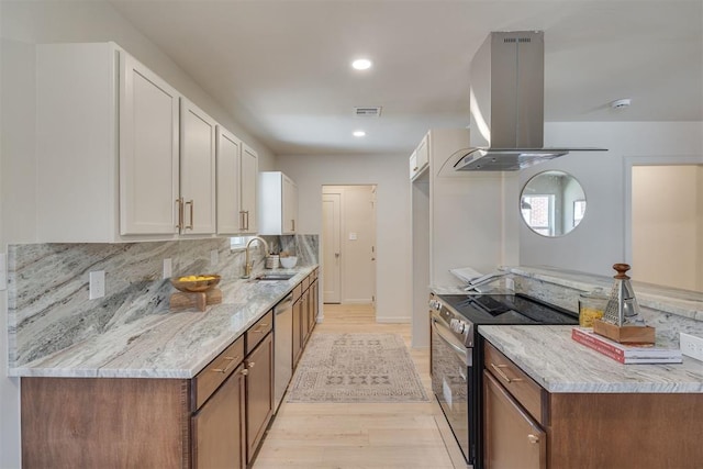 1109 NE 17th St, Oklahoma City, OK 73111 - kitchen with appliances with stainless steel finishes, island exhaust hood, light wood-type flooring, white cabinetry, and light stone counters