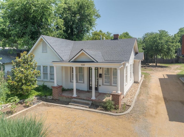 1134 NW 40th St, Oklahoma City, OK 73118 - view of front of home featuring roof with shingles, a porch, dirt driveway, and a chimney