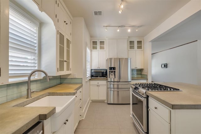1134 NW 40th St, Oklahoma City, OK 73118 - kitchen with appliances with stainless steel finishes, backsplash, white cabinetry, light tile patterned floors, and glass insert cabinets