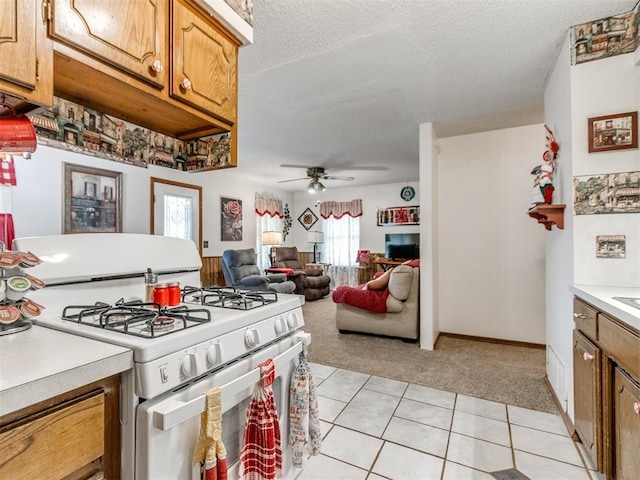 3900 Chetwood Dr, Del City, OK 73115 - kitchen with white range with gas stovetop, light colored carpet, light countertops, light tile patterned floors, and a ceiling fan