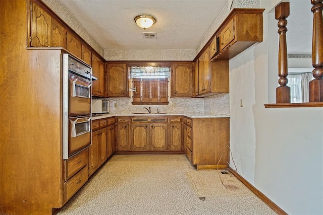 3913 SE 14th Pl, Oklahoma City, OK 73115 - kitchen featuring multiple ovens, brown cabinets, light countertops, a textured ceiling, and tasteful backsplash