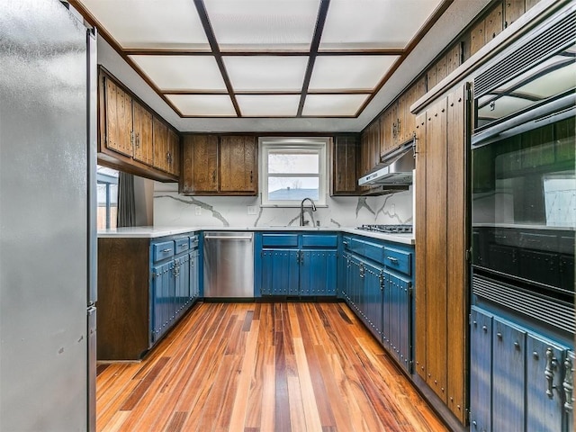 2912 Smiling Hill Blvd, Edmond, OK 73013 - kitchen with appliances with stainless steel finishes, blue cabinets, light wood finished floors, under cabinet range hood, and light countertops