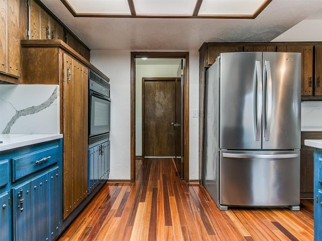 2912 Smiling Hill Blvd, Edmond, OK 73013 - kitchen featuring freestanding refrigerator, black oven, blue cabinets, wood finished floors, and light countertops