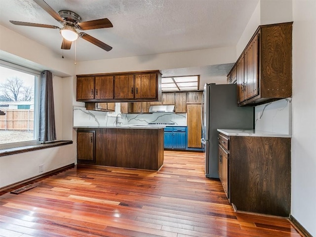2912 Smiling Hill Blvd, Edmond, OK 73013 - kitchen with a peninsula, under cabinet range hood, a ceiling fan, light wood-type flooring, and freestanding refrigerator