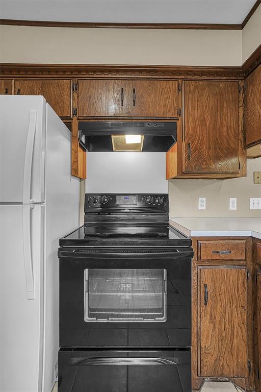 908 S Trail Dr, Altus, OK 73521 - kitchen featuring ventilation hood, freestanding refrigerator, black electric range, and brown cabinets