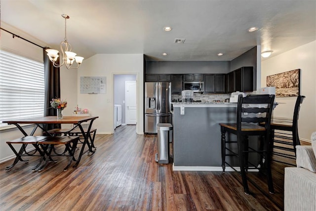 11704 NW 135th Ter, Piedmont, OK 73078 - kitchen featuring appliances with stainless steel finishes, dark wood-style flooring, a chandelier, a kitchen bar, and a peninsula