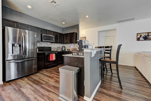 11704 NW 135th Ter, Piedmont, OK 73078 - kitchen with stainless steel appliances, a breakfast bar area, dark wood-style floors, decorative backsplash, and light stone countertops